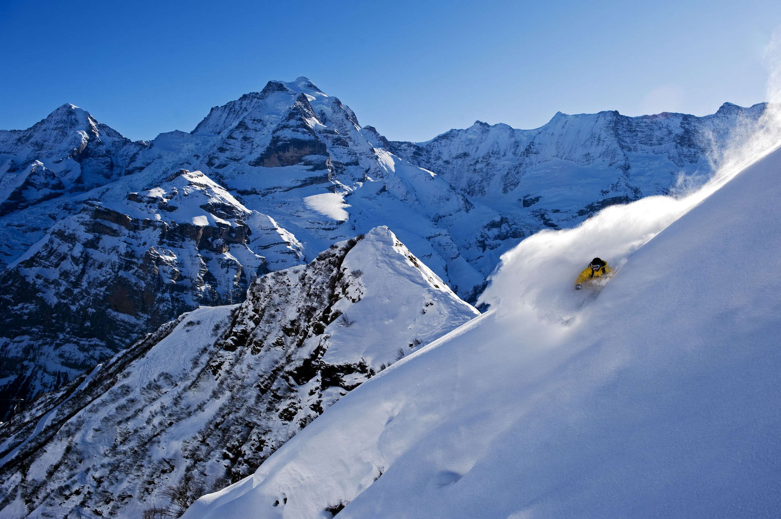 Der Skifahrer zieht frische Linien in den Pulverschnee im Skigebiet Mürren-Schilthorn. Das atemraubende Bergpanorama ist aus der Ferne zu sehen.