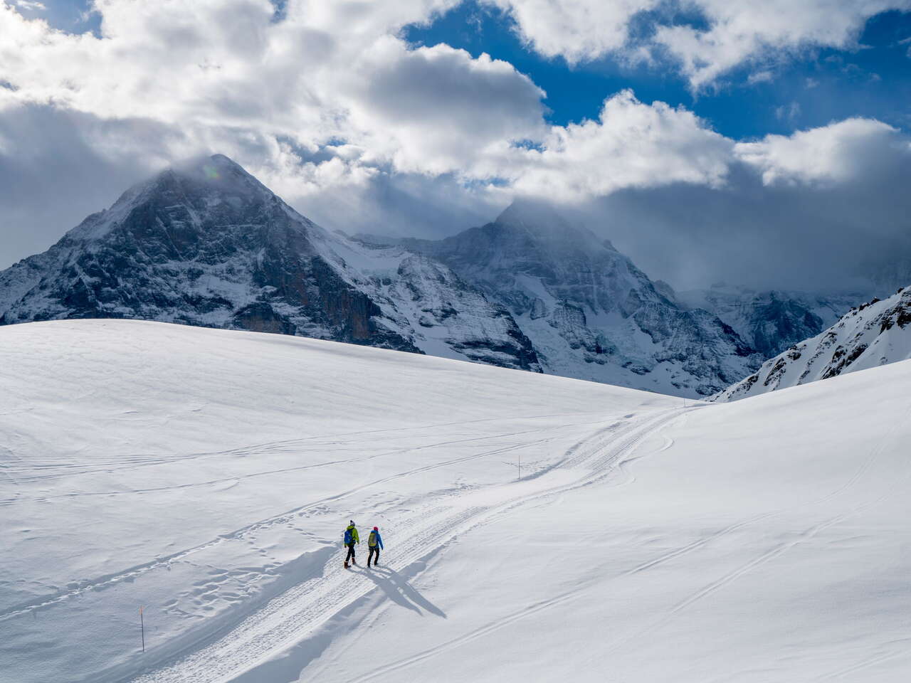 Winterwanderung auf verschneiten Winterwanderwegen rund um Grindelwald. Die Wanderer geniessen den sonnigen Tag und imposanten Ausblick auf den Eiger.